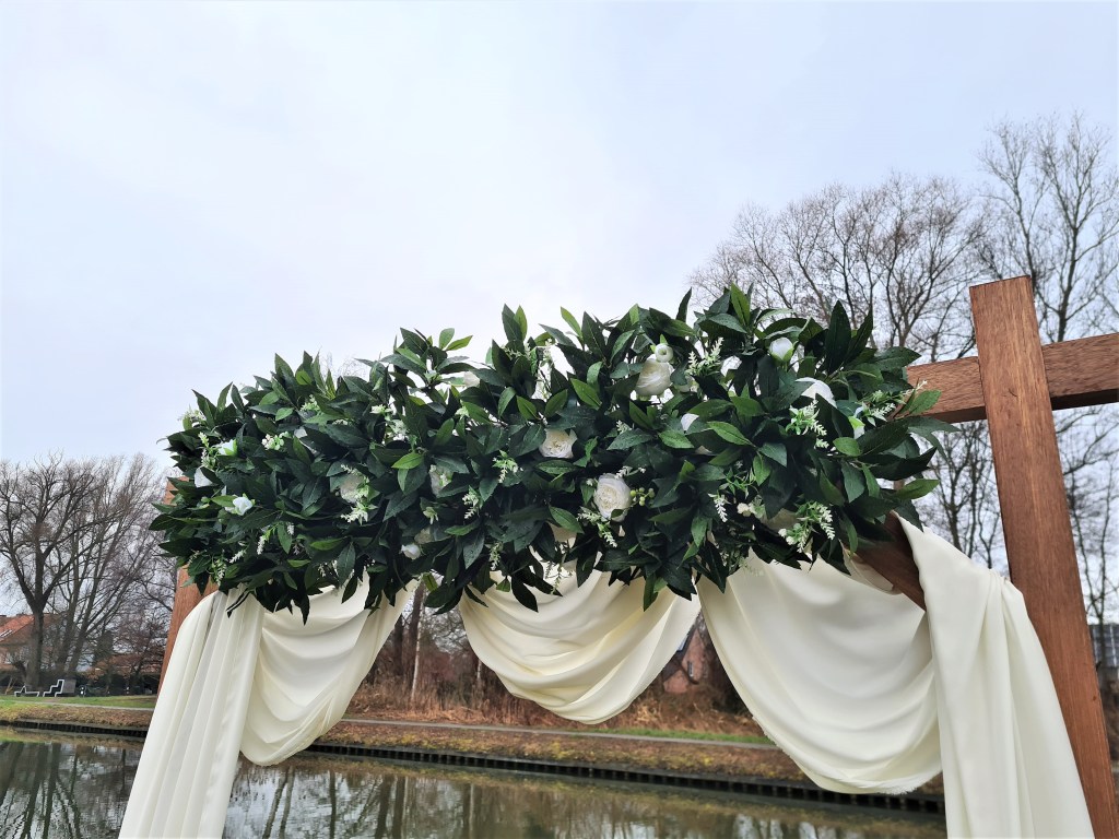 Detailaanzicht bloemen van decoratieboog White Dreams om te verhuren. Witte bloemen met groen er rond en witte doeken op een houten boog. 